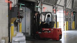 Lights in the upper corners of the interior dock doors confirm trailer restraint status as a forklift operator exits a trailer