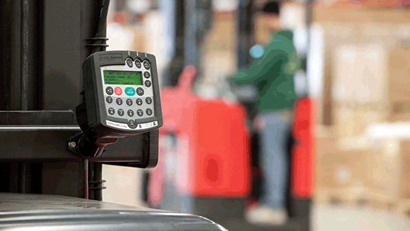 An operator drives a reachfork lift truck In the foreground fleet management software is ready for an operator to perform an automated operator checklist